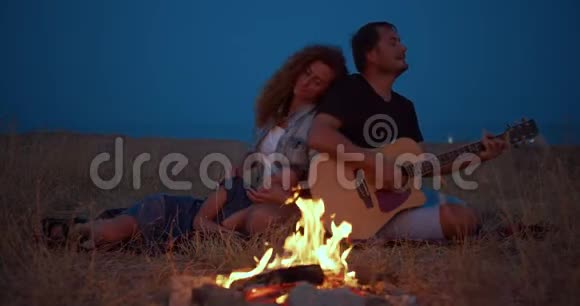 爸爸弹吉他妈妈和儿子在篝火旁放松家庭野餐特写镜头视频的预览图