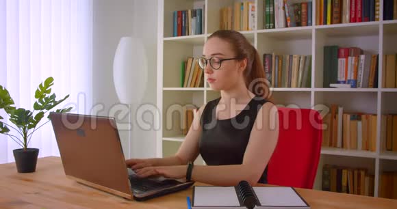 年轻漂亮的红发女商人戴着笔记本电脑的眼镜在办公室里看着照相机的特写照片视频的预览图