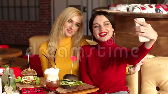 两个漂亮的年轻女孩坐在咖啡馆里吃汉堡包视频的预览图