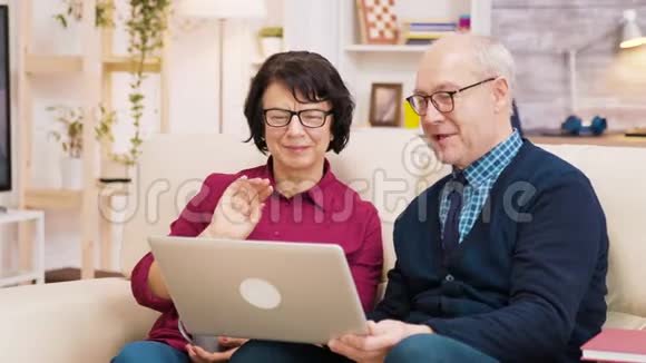 一对老年夫妇坐在沙发上拿着笔记本电脑在视频通话中视频的预览图