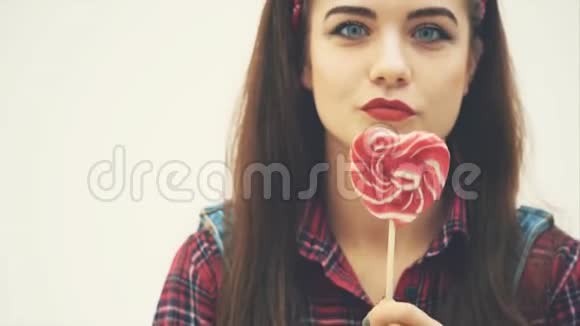 可爱迷人的女孩把她的嘴藏在红色的心形棒棒糖后面亲吻相机微笑视频的预览图