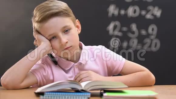 上数学课的时候一个无聊的小男孩坐在课桌前看着摄像机视频的预览图