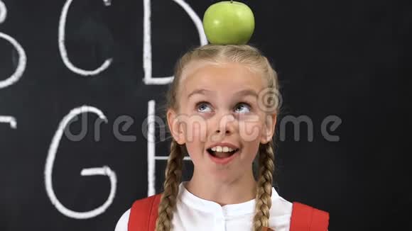 滑稽的小女孩头上戴着苹果黑板上写着字母视频的预览图