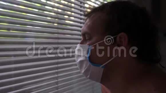 躺在医院房间里的戴防护口罩的悲伤的年轻人看着窗户百叶窗慢动作视频的预览图