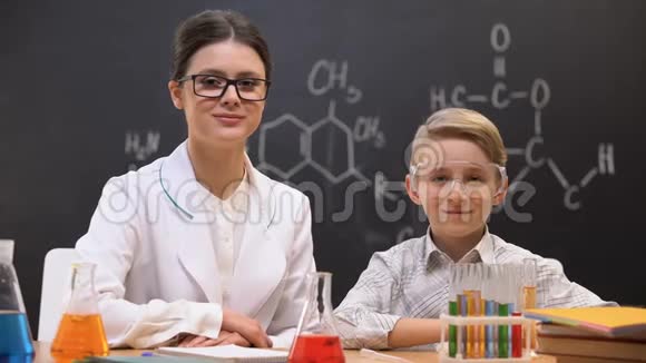小男孩和老师对着镜头看化学课实验室视频的预览图