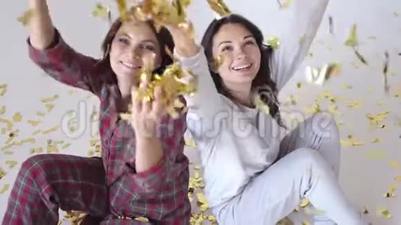 美丽的快乐女孩在白色的背景上投掷金色闪光的纸屑慢动作视频的预览图