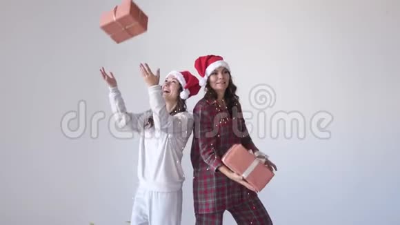 穿着圣诞帽和睡衣的快乐女孩在白色背景下扔礼物盒等待节日视频的预览图