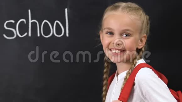 小女孩背着背包对着镜头微笑学校的字写在黑板上视频的预览图