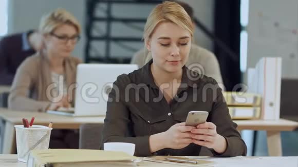 年轻漂亮的快乐女人坐在工作的地方微笑着使用智能手机视频的预览图