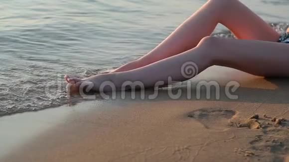 穿着泳装坐在海边潮湿的沙滩上的年轻女孩视频的预览图