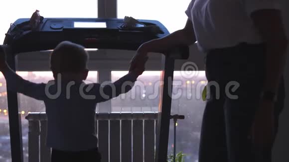 有趣的小孩在现代跑步机上行走妈妈把他的手放在大窗户旁边视频的预览图