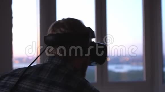 男人戴着虚拟现实的头盔背景是工作场所办公室的一扇巨大的窗户视频的预览图