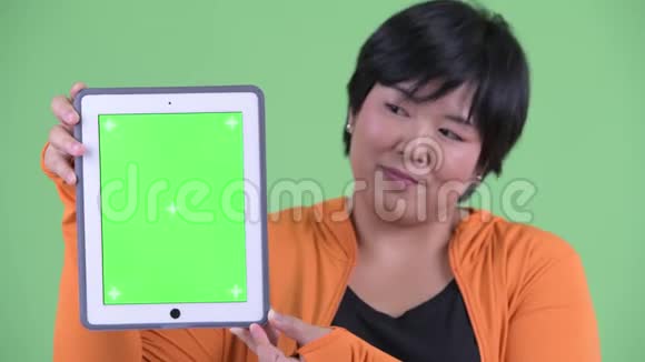 一位年轻体重超重的亚洲女性脸上挂着数码平板电脑准备去健身房视频的预览图