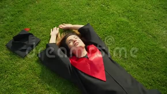 快乐微笑的女孩的肖像穿着黑色和红色的斗篷躺在草地上享受着她的自由年轻女子庆祝视频的预览图