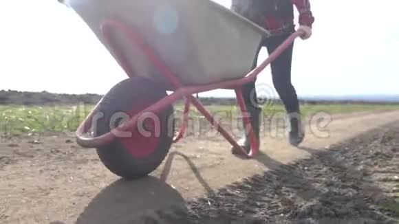 农民女孩红色生活方式的脖子工作在泥土的领域与花园手推车在橡胶靴农民生态农业视频的预览图