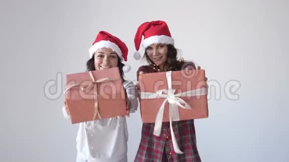 穿着圣诞帽和睡衣的年轻漂亮女人在白色背景上送礼物盒女人手里的小礼物视频的预览图