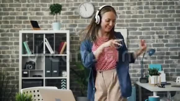 可爱的女孩在办公室里玩跳舞听着耳机里的音乐休息视频的预览图