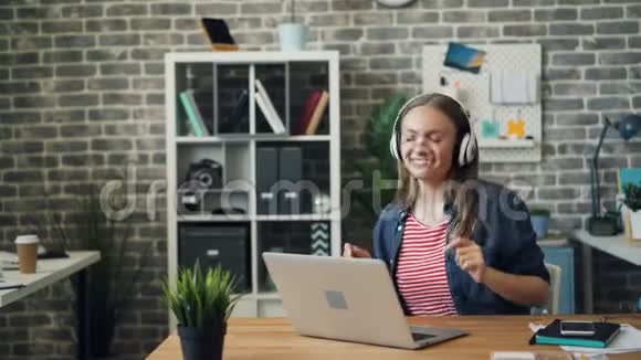 戴着耳机听音乐的漂亮女士在办公室跳舞举起手臂视频的预览图