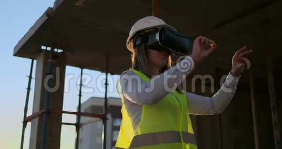 日落时分建筑屋顶上的女工程师戴着VR眼镜用手移动视频的预览图
