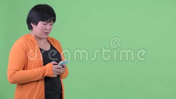 快乐的年轻超重的亚洲女人正在等着用手机准备健身房视频的预览图
