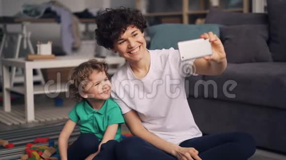 年轻的母亲和小儿子在公寓里用智能手机拍照视频的预览图