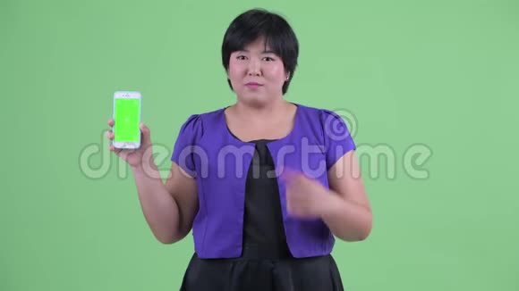 快乐的年轻超重的亚洲女人带着电话竖起大拇指视频的预览图