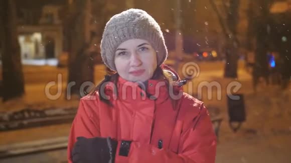 美丽的快乐女孩在夜间冬天的城市吹雪的肖像女人看着镜头视频的预览图