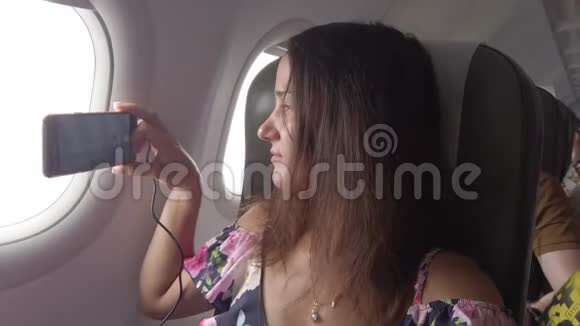 优雅的女人坐在飞机里看着舷窗在手机上拍照3840x2160视频的预览图
