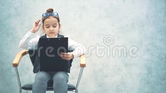 一个小女老板坐在椅子上有一个黑色的文件夹灰色背景特写戴眼镜读文件夹视频的预览图