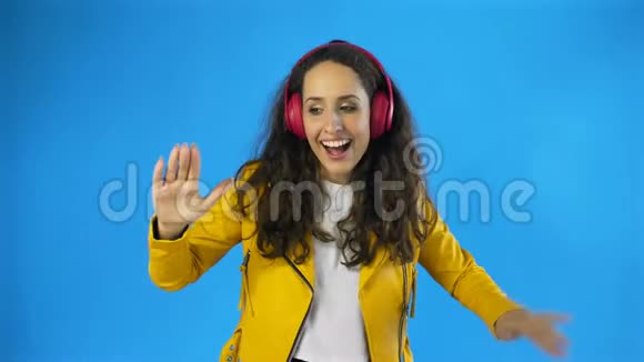 女士听音乐与红色耳机在工作室与蓝色背景视频的预览图