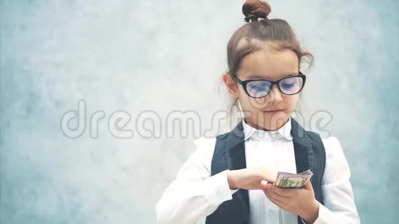 一幅幸福的女孩拿着一堆钞票感到满意的肖像看着摄像机被隔离在灰色的视频的预览图