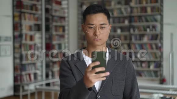 在书架背景上打电话发短信的亚洲年轻人视频的预览图