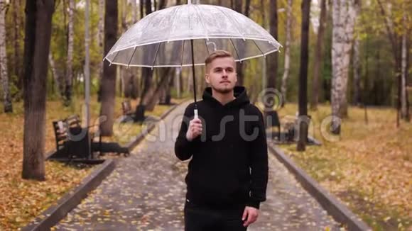 一个带着雨伞的年轻人在雨天沿着秋天公园散步的肖像视频的预览图