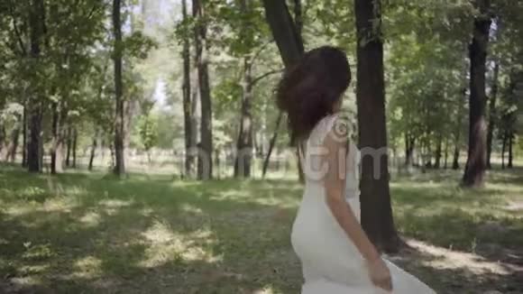迷人的年轻女孩穿着白色的长夏礼服在公园里旋转一个漂亮女人在户外休闲慢慢视频的预览图