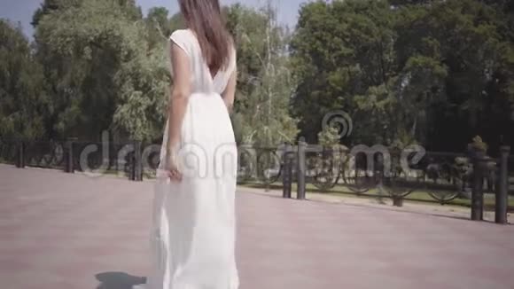 迷人的年轻女孩一头长长的黑发戴着太阳镜穿着一件白色的夏季时装长裙走在下面视频的预览图