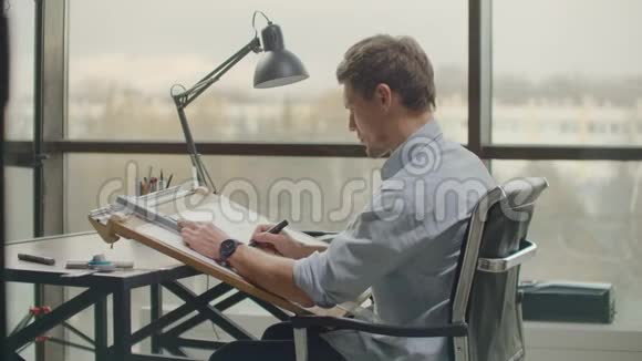 一位男性建筑师坐在一张桌子旁画出一个建筑的平面图从事设计开发坐在视频的预览图