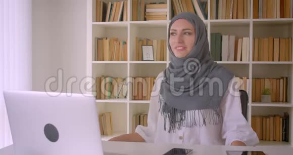 年轻漂亮的穆斯林女商人戴着头巾坐在办公室笔记本电脑前跳舞的特写照片视频的预览图
