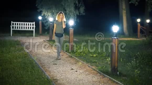 一个身材苗条甜美的中年妇女一头金发在一个夏天的傍晚带着灯笼走在一条绿色的小巷里视频的预览图