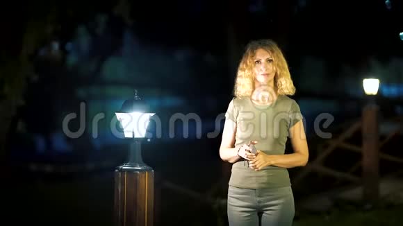 一个身材苗条甜美的女人一头金发中年在夏天的深夜站在一条明亮的街道上视频的预览图