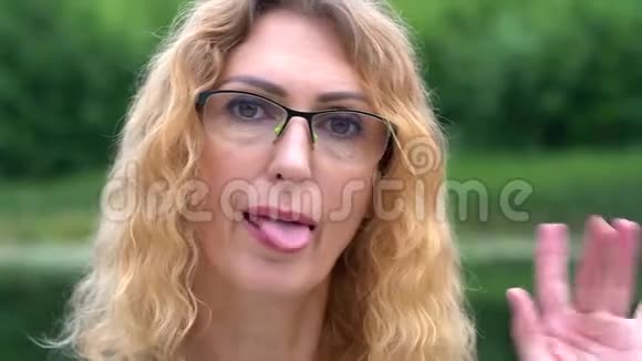 一个戴着眼镜金发碧眼的可爱中年妇女正在四处闲逛在大自然中露出舌头和微笑视频的预览图