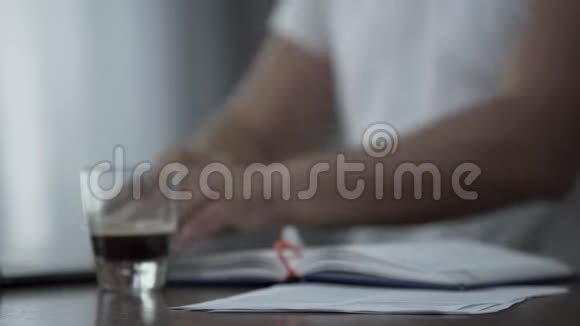 穿着白色t恤的男人在家里或办公室里拿着文件和喝咖啡他在研究视频的预览图