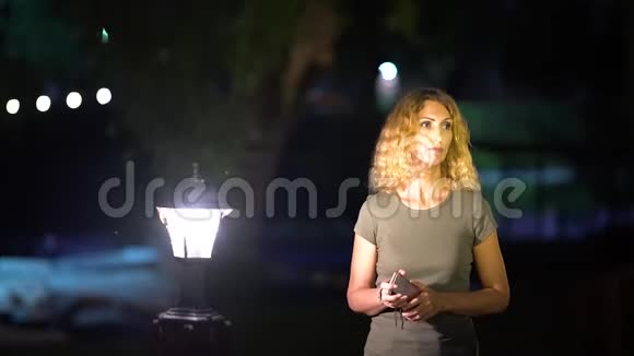 一个身材苗条的悲伤的女人一头金发中年在夏末一个明亮的灯笼附近打电话视频的预览图