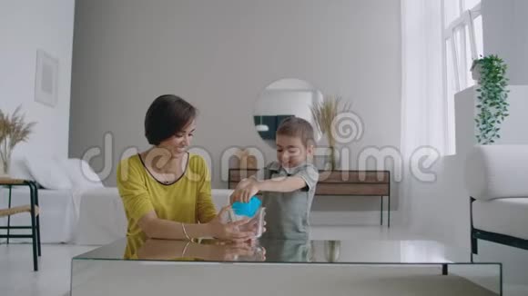 妈妈和儿子坐在地板上玩桌子用弹性玩具笑视频的预览图
