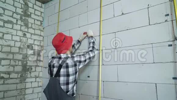 建筑工人在工作中的磨损和红帽将施工夹插入砌块墙中视频的预览图