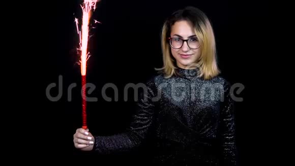 女孩手里拿着烟花一个年轻的女人站在黑色背景上穿着一件闪亮的晚礼服4k视频的预览图