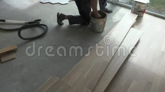 无法辨认的工人在混凝土地板上涂胶水橡木地板铺设视频的预览图