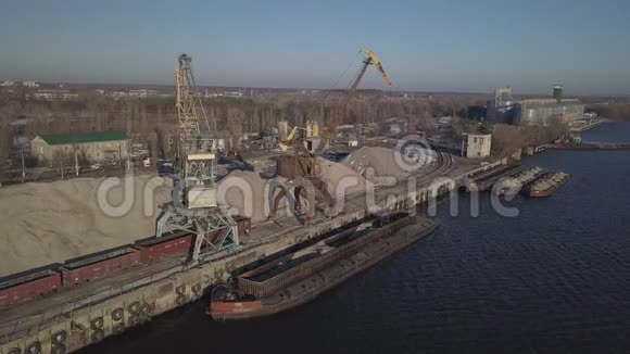 码头附近岸边的大型港口起重机将河沙驳船卸到一大堆上运输的火车视频的预览图