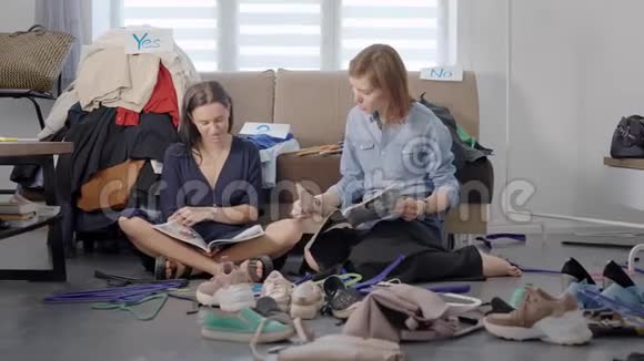 两位朋友上演了家庭衣柜和疲惫的分析女人坐在地板上看时尚视频的预览图
