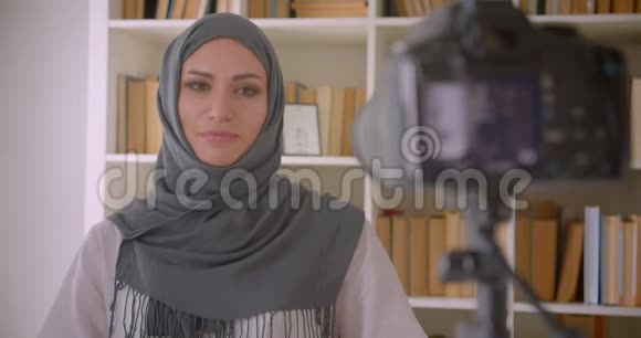 年轻有魅力的穆斯林博客写真者戴着头巾在室内用相机做手势视频的预览图
