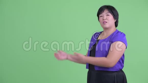 快乐年轻体重超重的亚洲女人向后展示一些东西视频的预览图